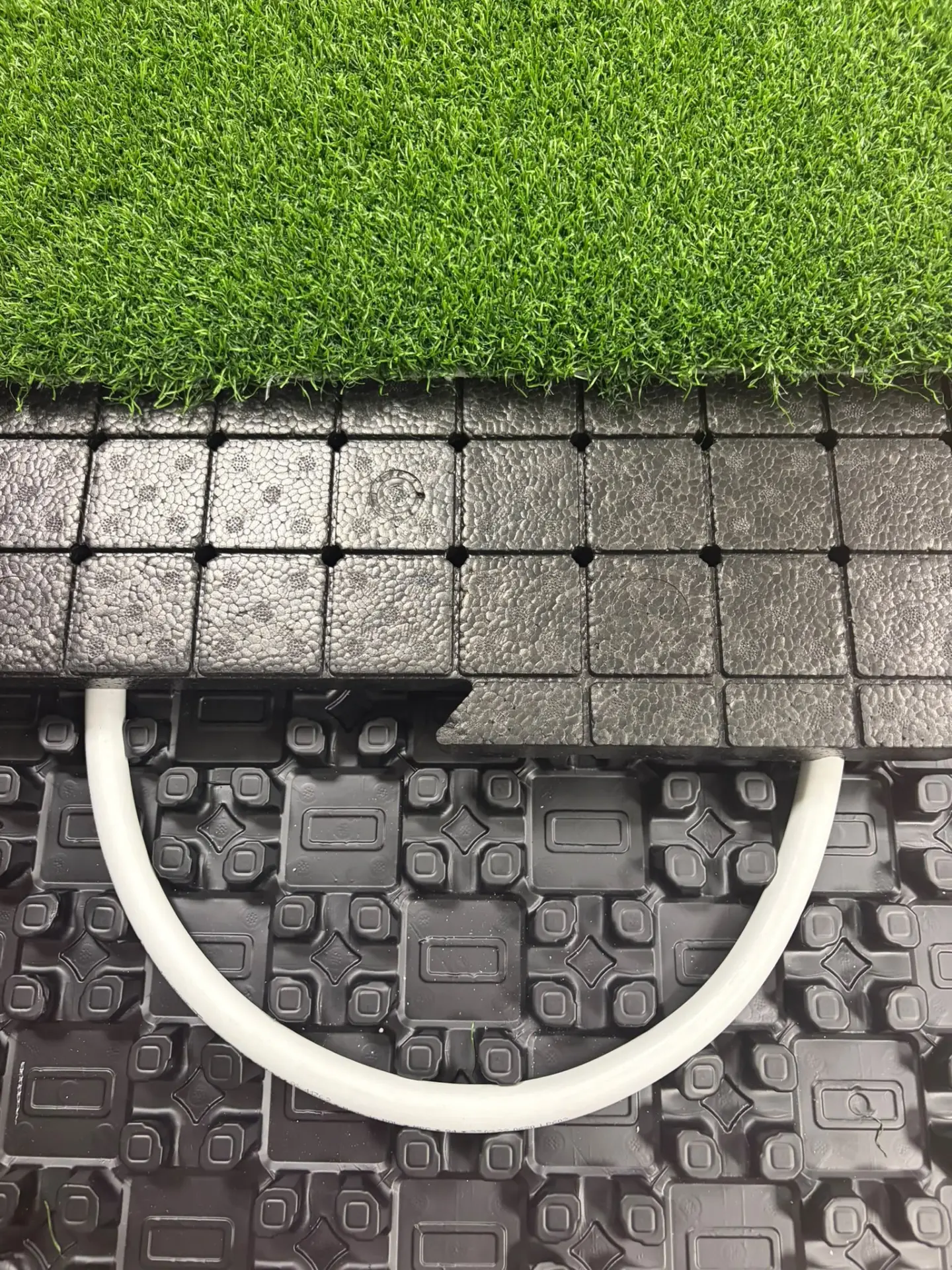 Detail van de opbouw: kunstgras, shockpad-tegels en de HeatReady-leiding in de drainageplaat